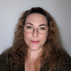 Frau mit lockigem, dunkelblondem Haar und Brille, lächelt in die Kamera.