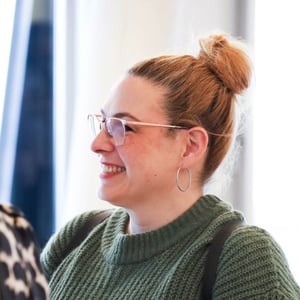 Eine lächelnde Frau mit Brille und einem blonden Dutt, gekleidet in einem grünen Pullover. Eine lächelnde Frau mit Brille und einem blonden Dutt, gekleidet in einem grünen Pullover.