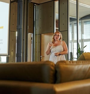 Blonde Frau in weißem Kleid steht in einem modernen Raum mit Glas und Holz und redet gestikulierend. Blonde Frau in weißem Kleid steht in einem modernen Raum mit Glas und Holz und redet gestikulierend.