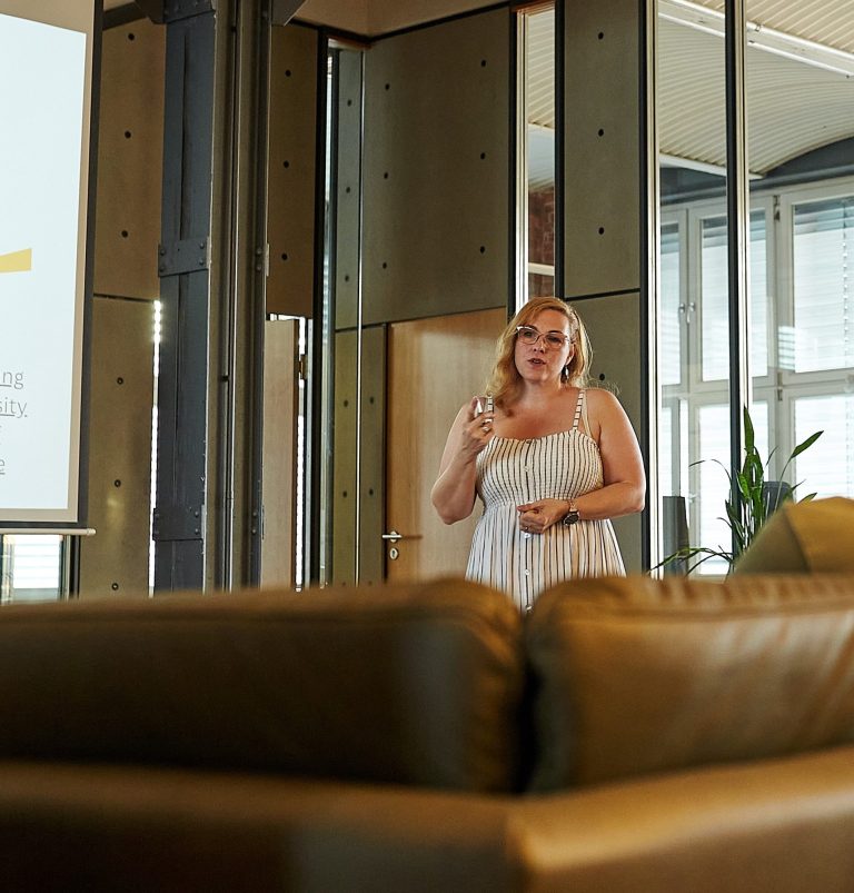 Frau in weißem Kleid steht in einem modernen Raum mit Glas und Holz.