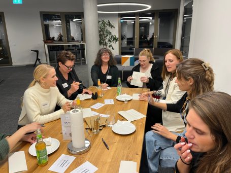 Eine Gruppe von Menschen sitzt an einem Tisch und kommuniziert bei Snacks und Getränken.